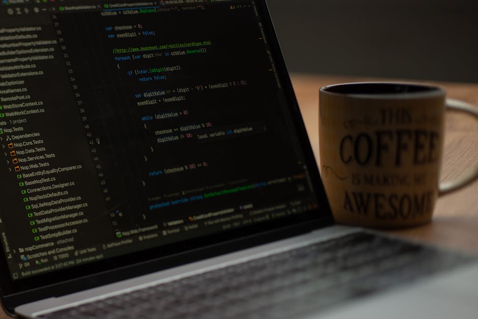 A close-up photograph of a laptop displaying lines of programming code on a dark background, with illuminated syntax highlighting in green, blue, and orange. To the right of the laptop, there is a cer